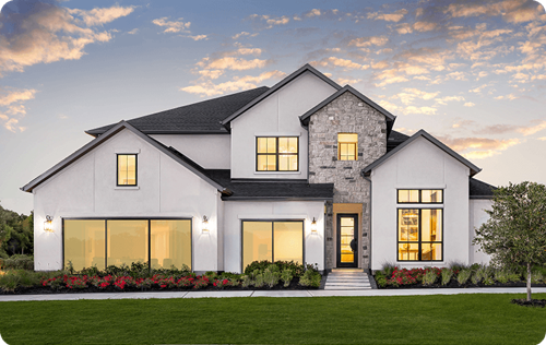 Toll Brothers home at Midline at dusk, with white stucco exterior, stone accent facade, large glass windows, and a landscaped front entry.