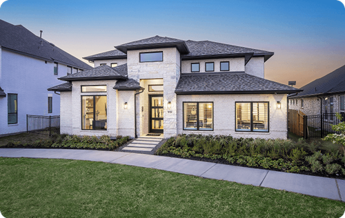 Perry Homes home at Midline at dusk, with white brick exterior, modern hip roofline, large front windows, and a curved front walkway.